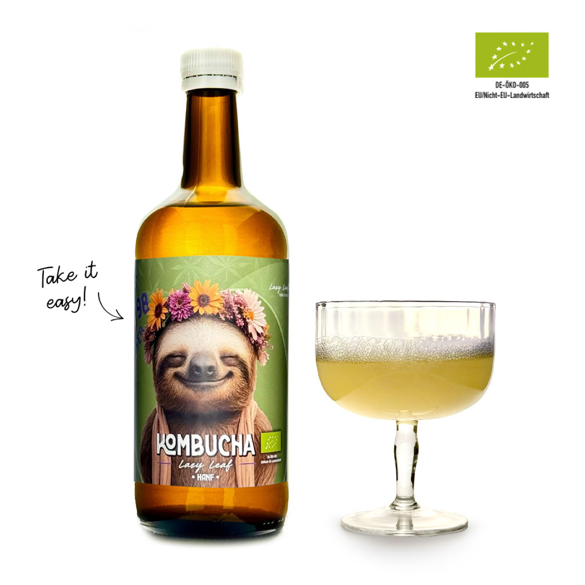 Eine braune Flasche mit einem Etikett, das ein Faultier mit Blumenkranz zeigt, steht neben einem Glas mit hellgelber Flüssigkeit. Oben rechts ist ein Bio-Siegel zu sehen.