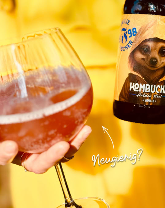 Eine Hand hält ein Glas mit einem Getränk, daneben eine Flasche mit einem Etikett, das ein Tier zeigt.