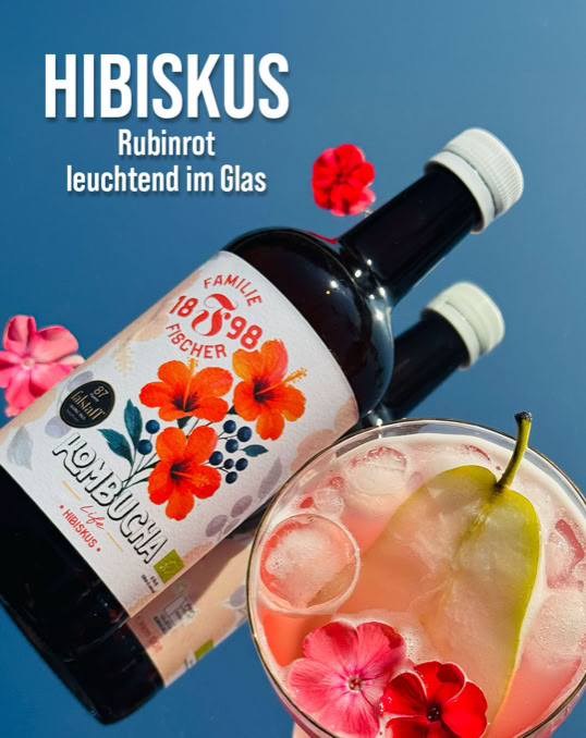 Zwei Flaschen mit Hibiskus-Getränk und ein Glas mit einer Birnenscheibe und Hibiskusblüten, vor blauem Hintergrund.