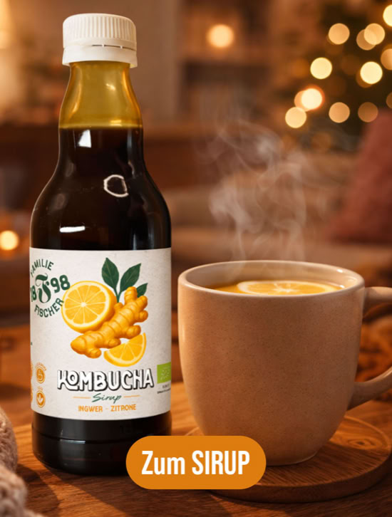 Kombucha Sirup und Tasse mit dampfendem Getränk auf einem Tisch, im Hintergrund unscharfe Lichter.